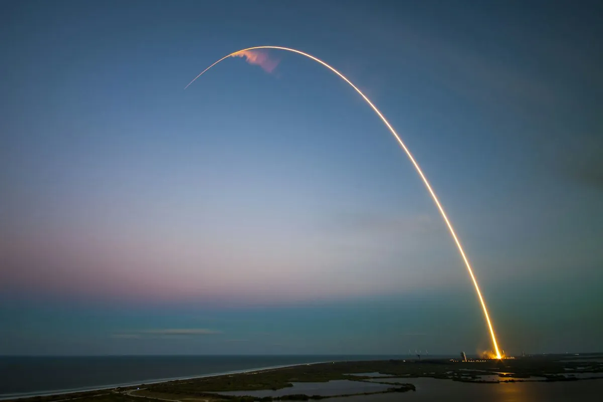 A rocket climbing into the sky at dusk, leaving a trail of light